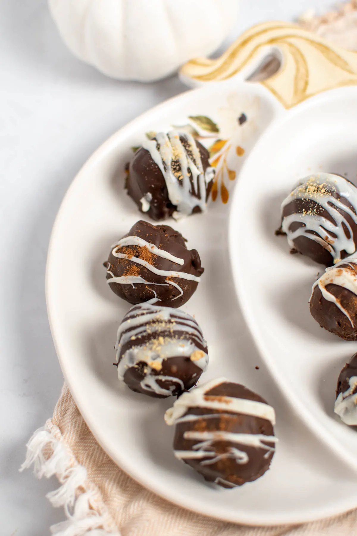 Several pumpkin pie truffles with white chocolate drizzle on pumpkin platter.