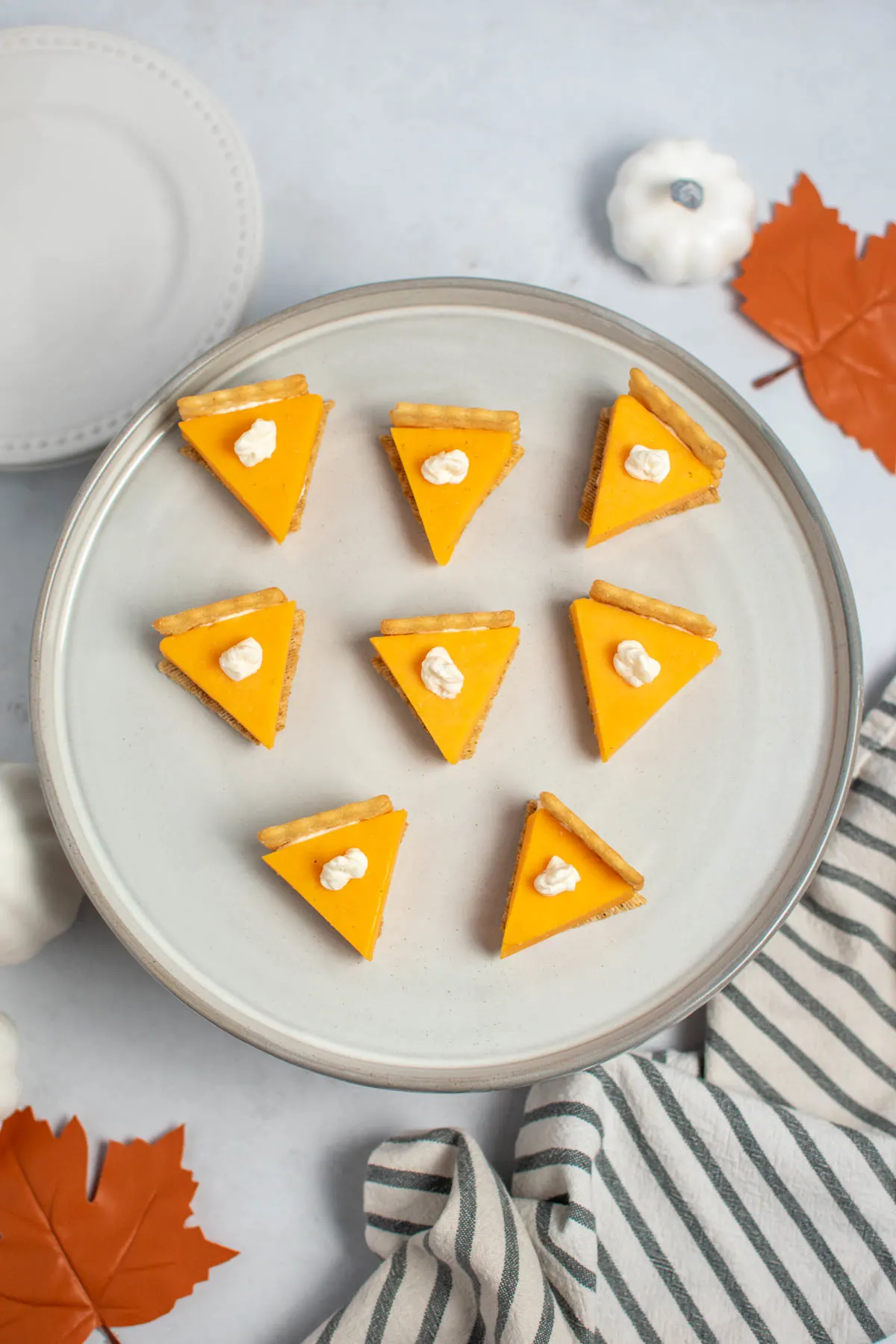 Several cheese and cracker pumpkin pie bites on gray cake stand.