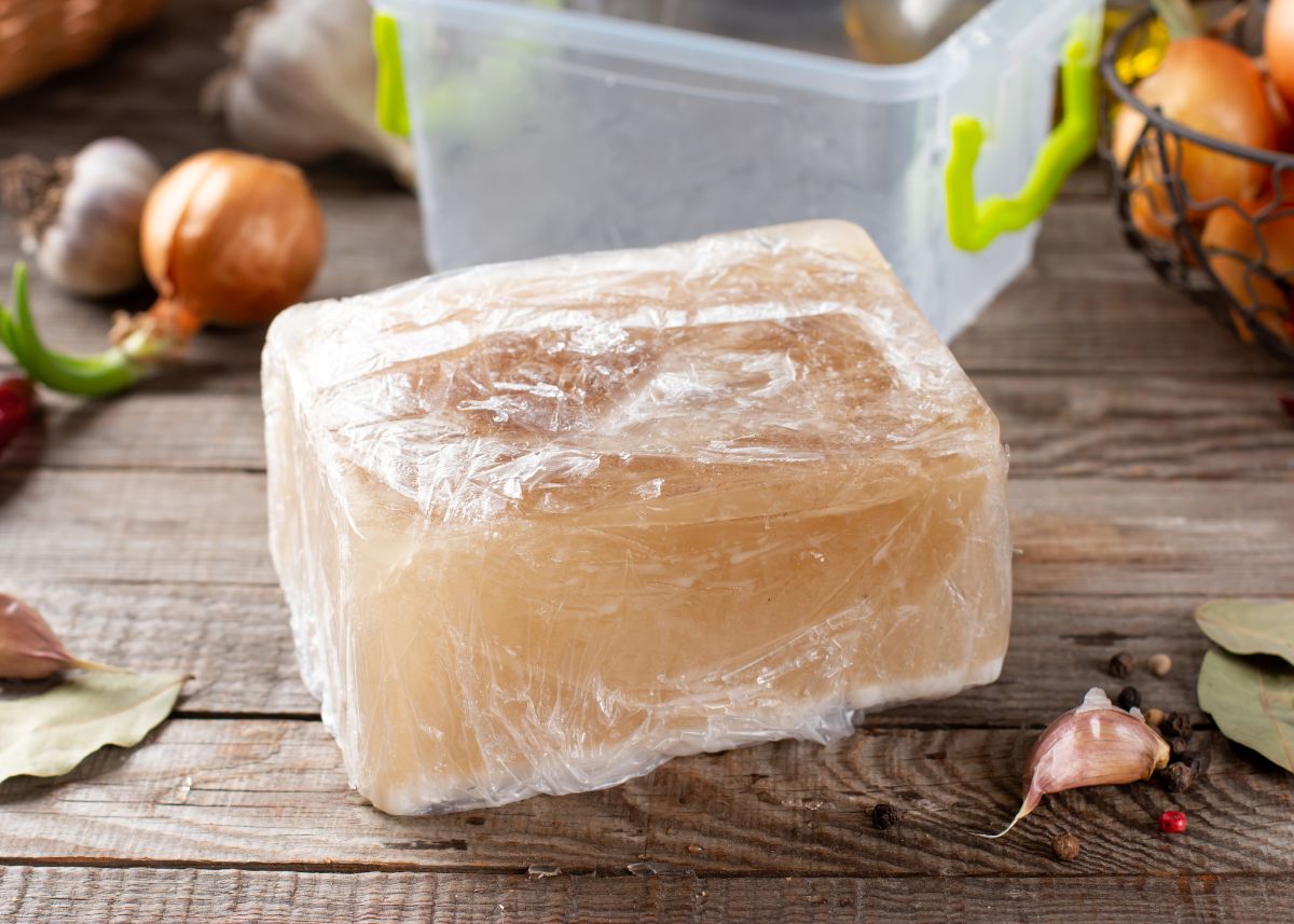 A large block of frozen broth on a wooden table next to tupperware.