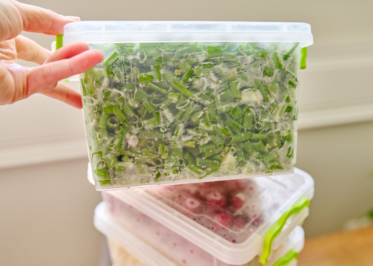 A woman holds up a clear container filled with frozen diced green onions.