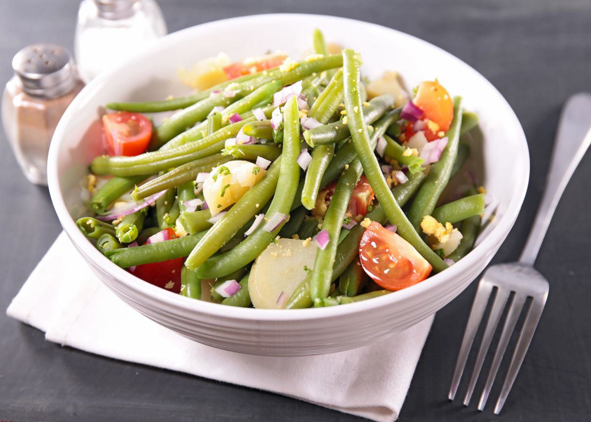 Fresh green bean salad with onions, tomatoes, and water chestnuts in a white bowl.