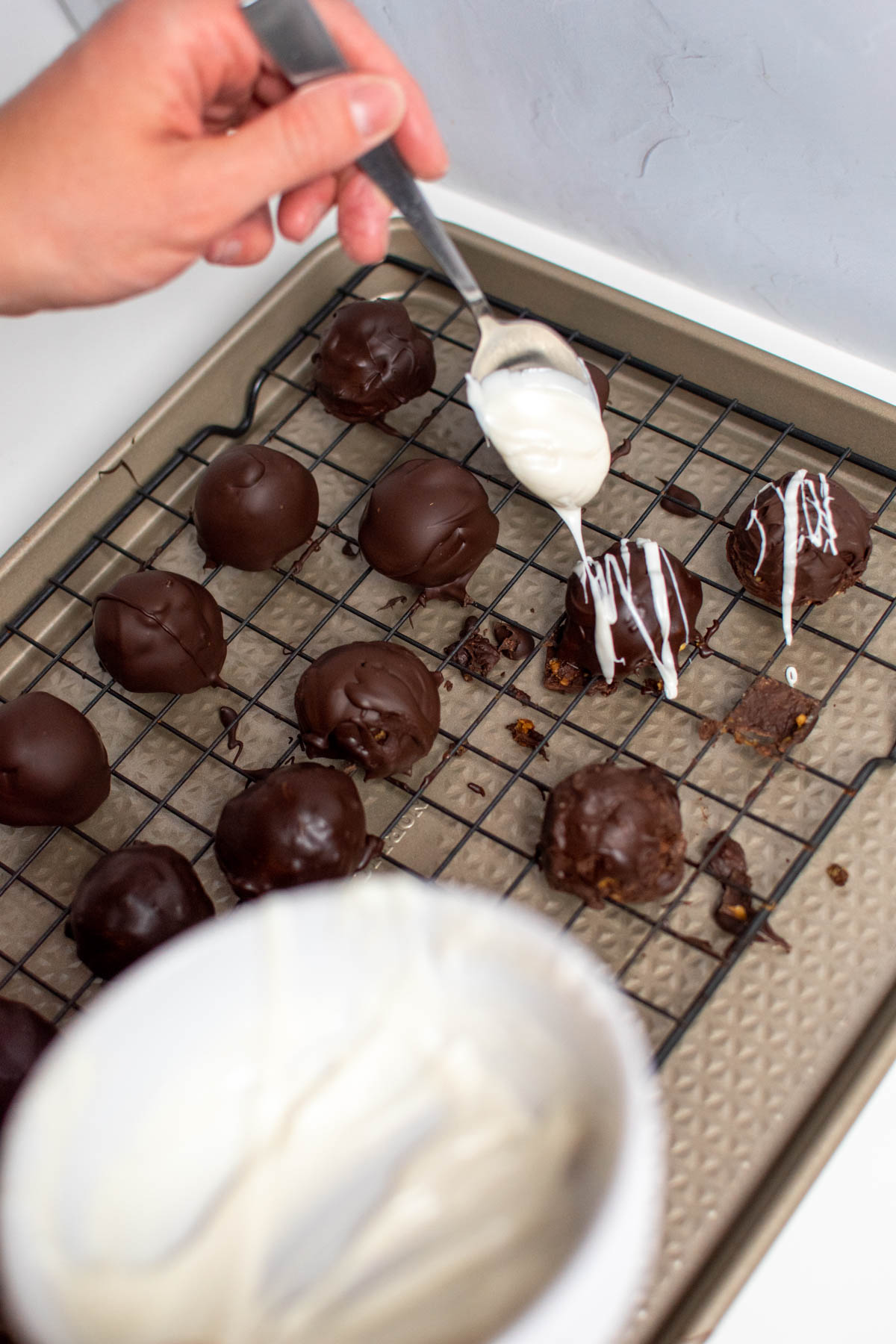 Woman's hand drizzles white chocolate from spoon onto chocolate truffles.