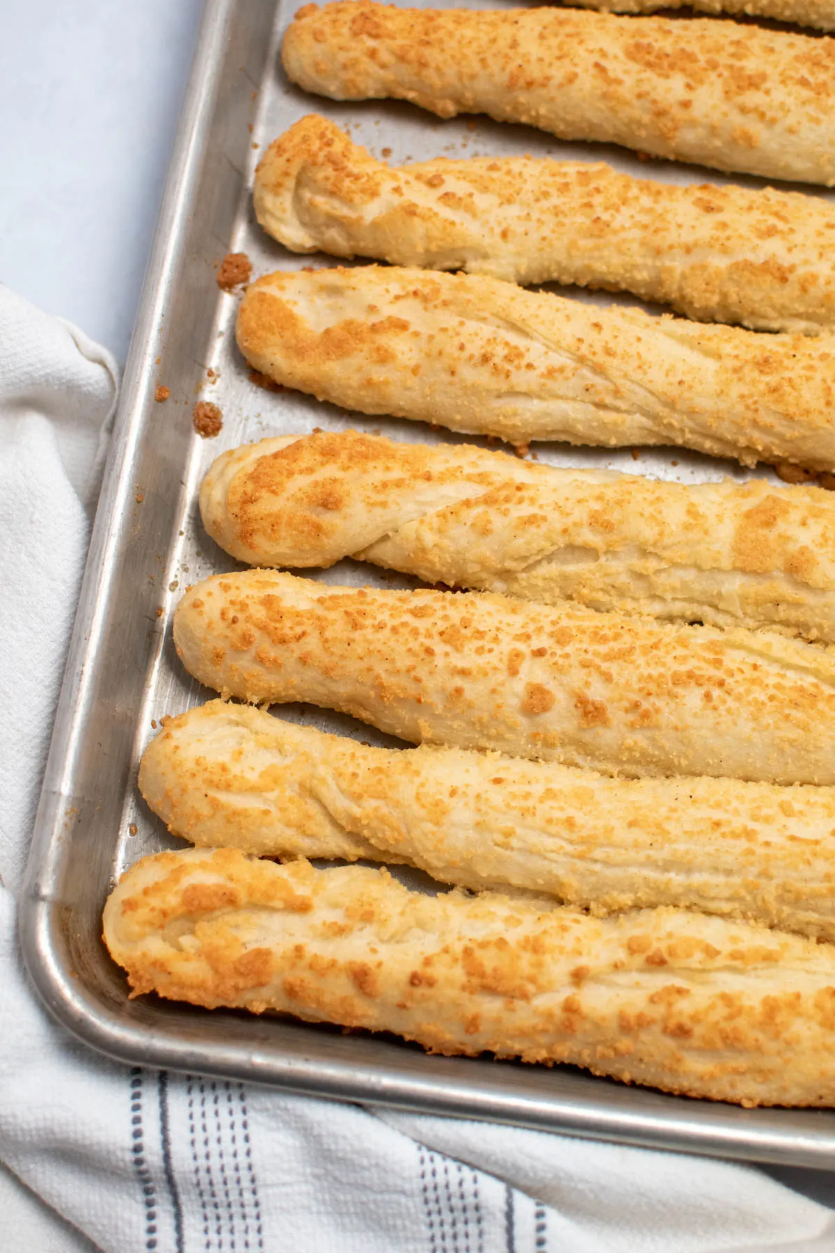 Several homemade breadsticks with parmesan cheese on metal baking sheet.