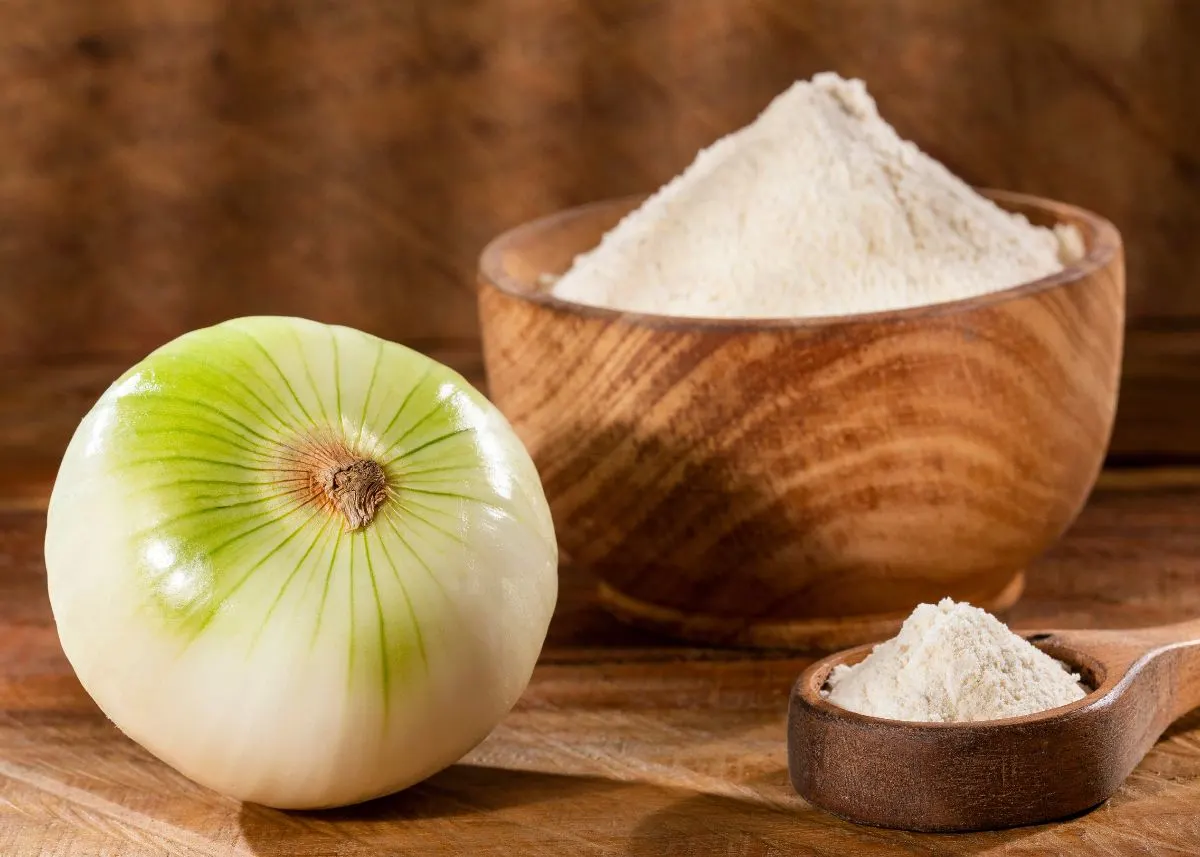 A whole white onion next to two wooden bowls of onion powder.