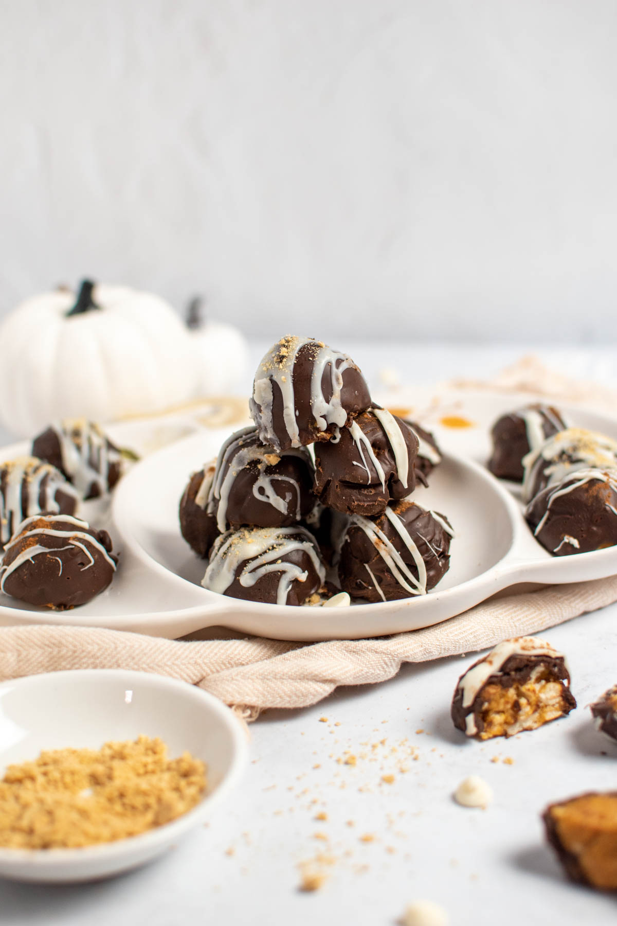 Pumpkin spice truffles stacked on white platter with various ingredients in the foreground.