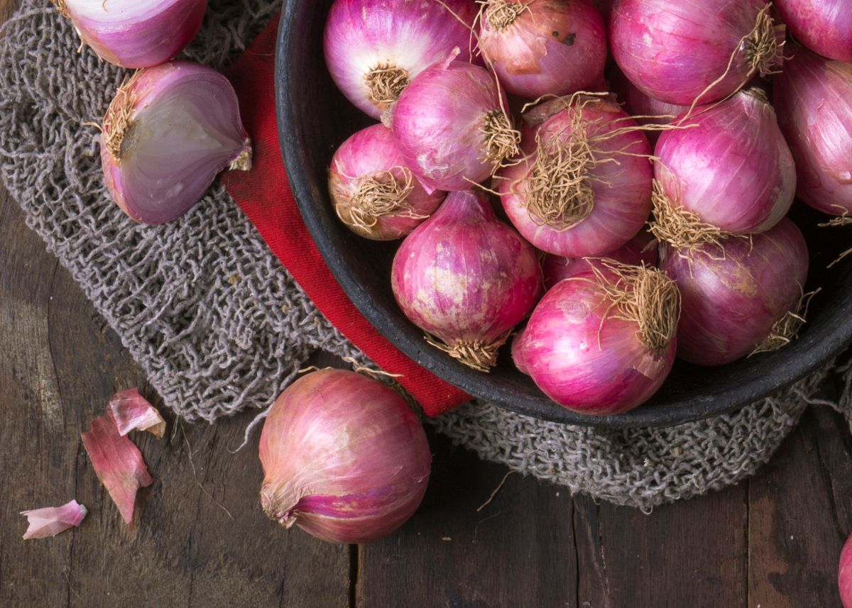 Wooden basket filled with whole unpeeled red onions over a burlap cloth.