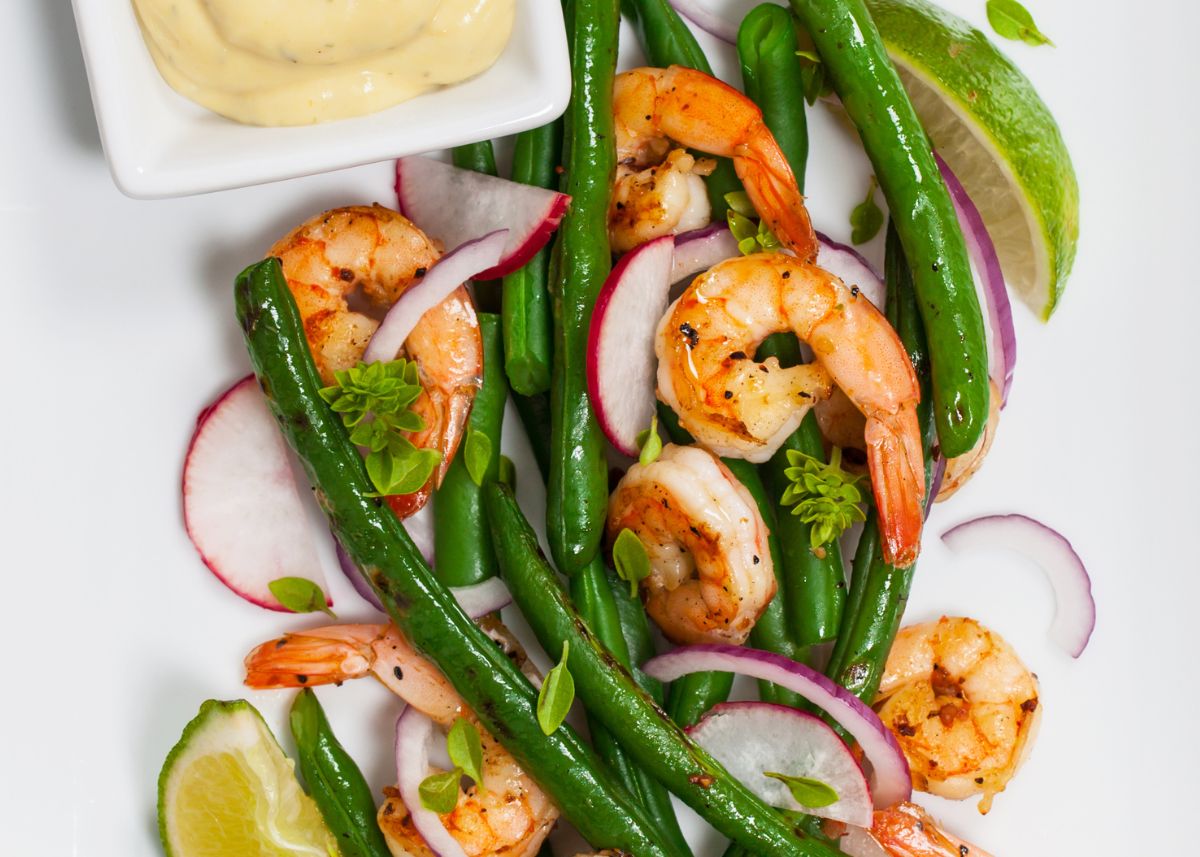 Grilled shrimp with green beans, radishes, red onion, and lime on a white plate.