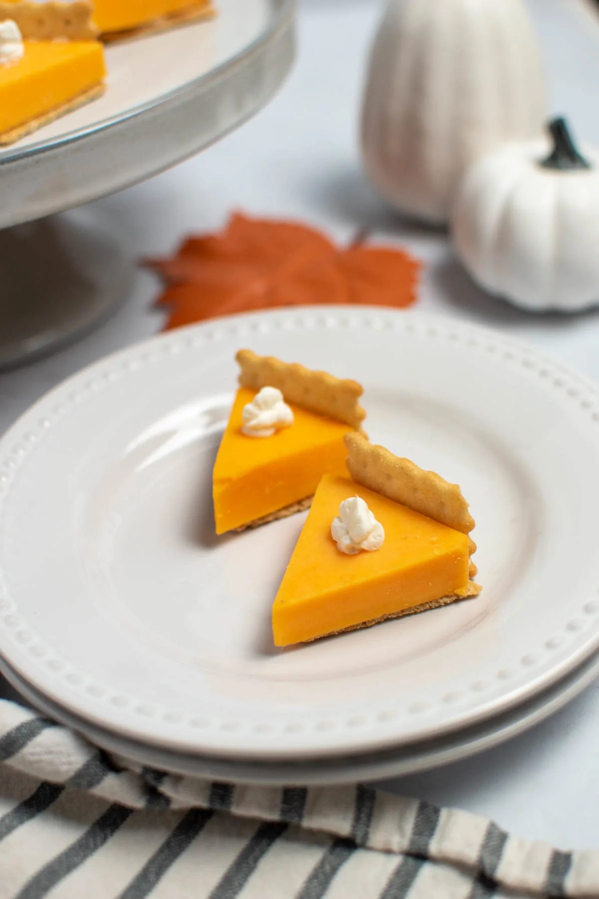 Thankgiving cheese and cracker appetizer on white plate with fake pumpkins in background.