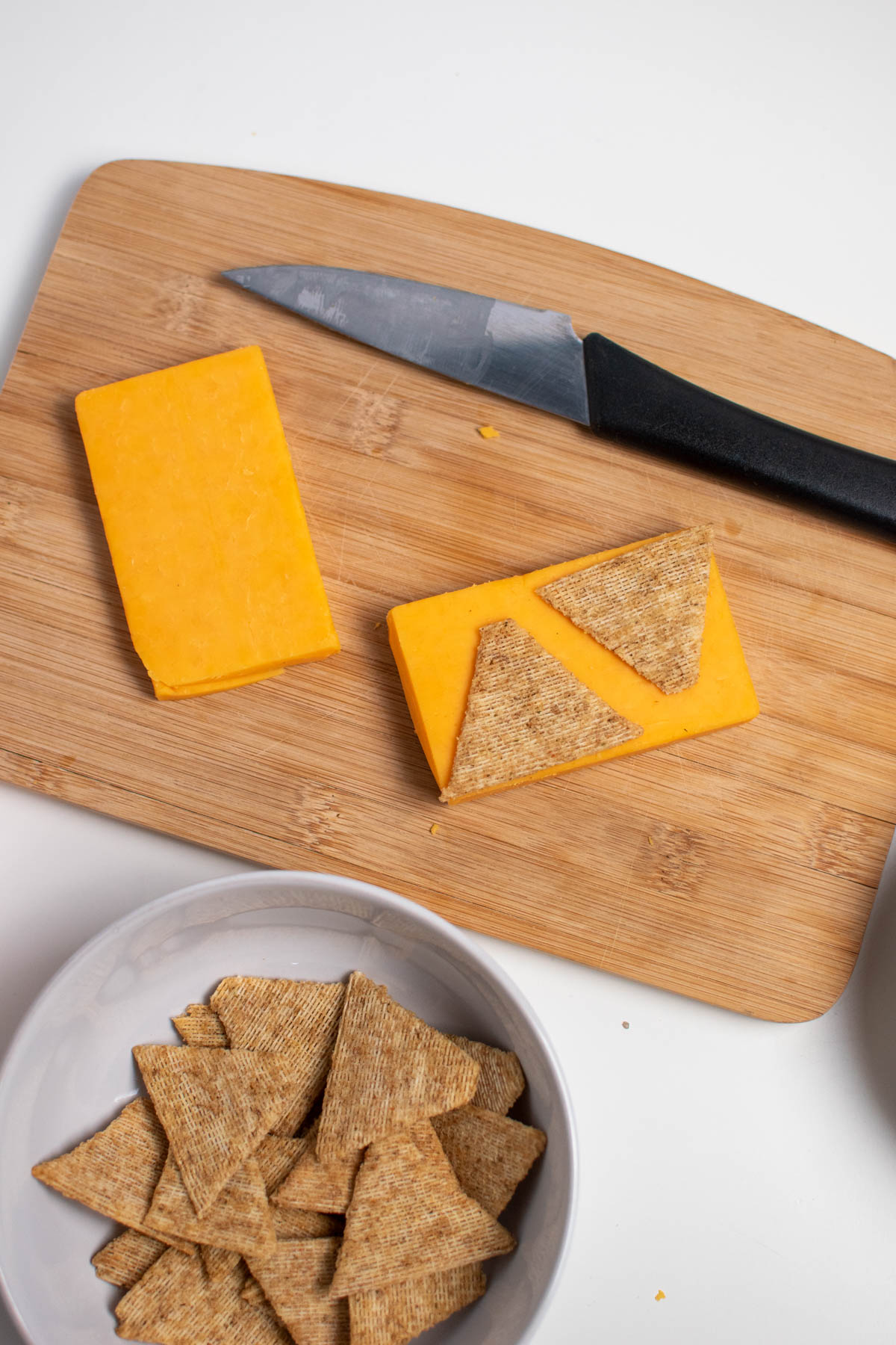 Two Triscuit crackers on a rectangle of cheddar cheese all on wood cutting board.