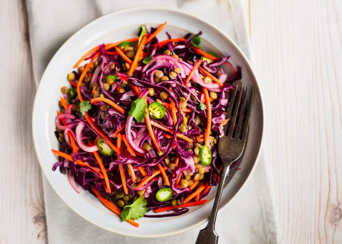 Asian cabbage slaw on a white plate with carrots, red onion, and cilantro.