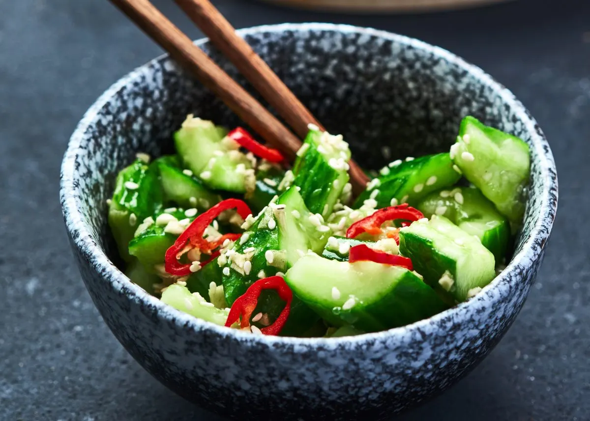 A gray and white speckled bowl with Asian cucumber salad and chopsticks.