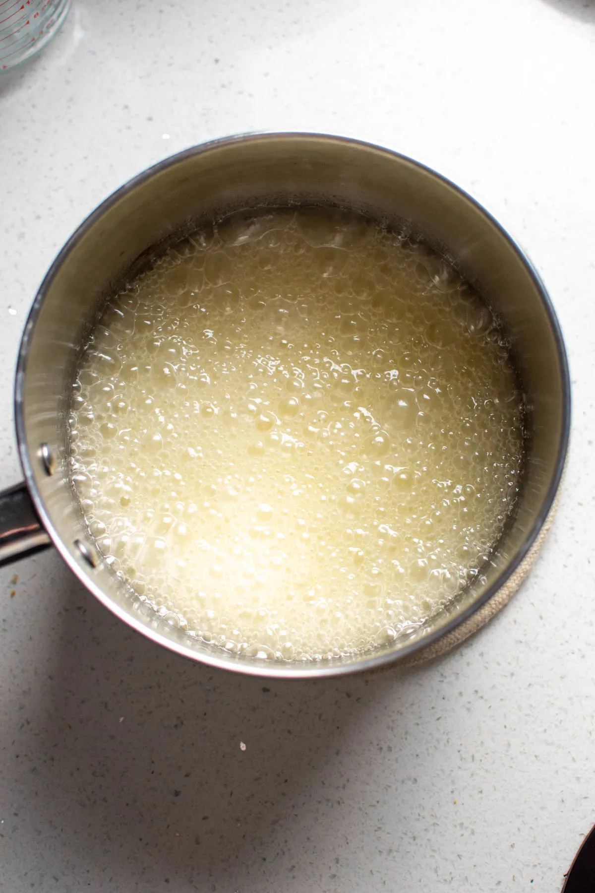 Metal saucepan with boiling sugar syrup on quartz countertop.
