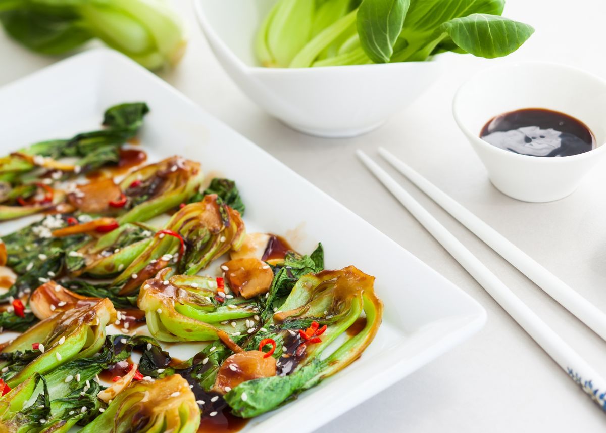 Baked Bok Choy with Asian sauce on a white platter next to chopsticks.