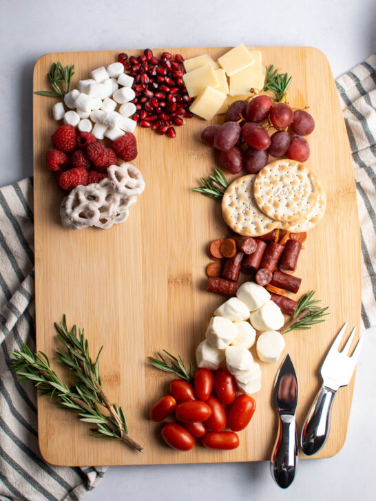 Candy cane charcuterie board with different red and white food and fresh rosemary on table.
