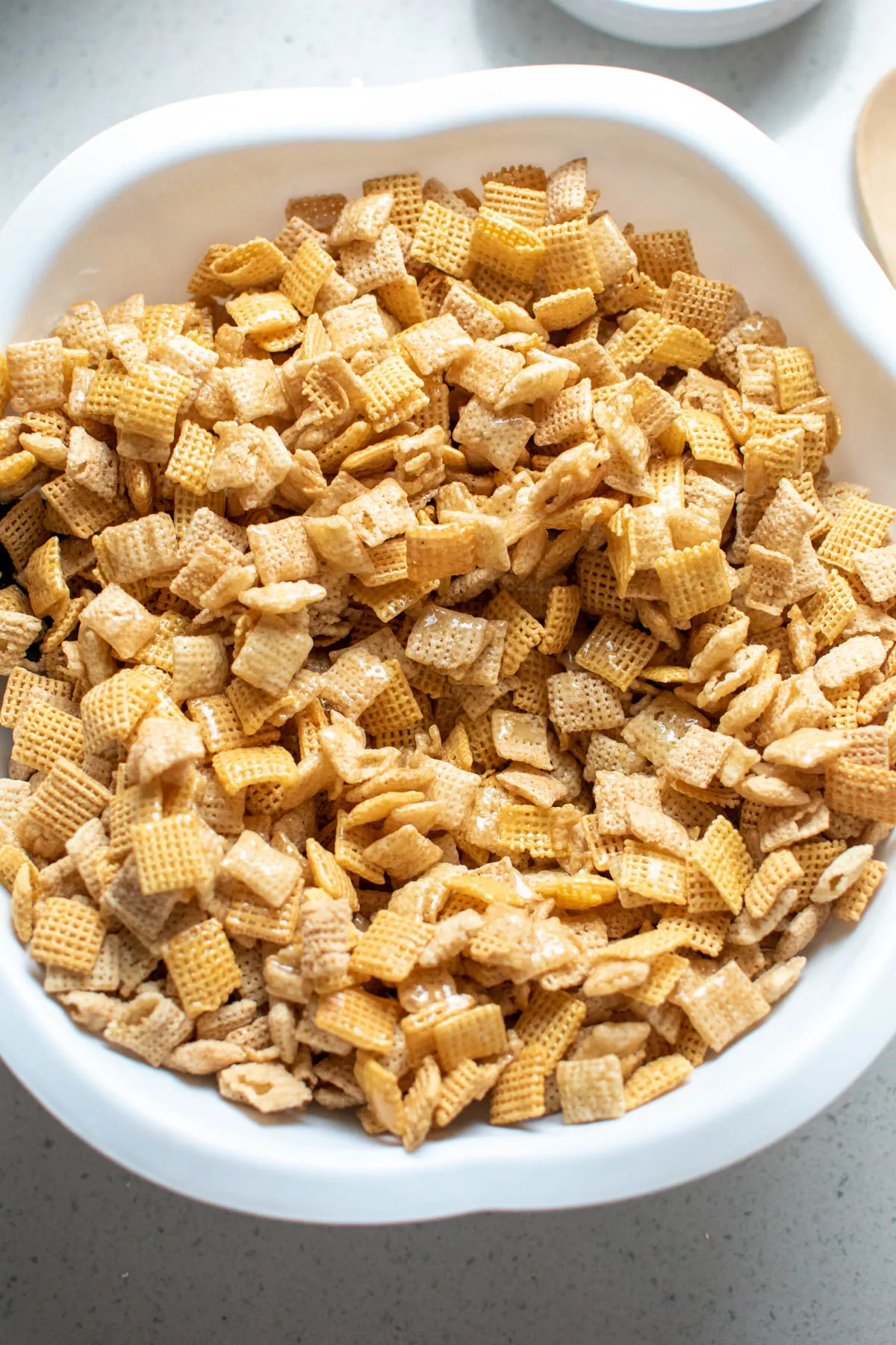 Large white bowl with Chex mix covered in sugar syrup on countertop.