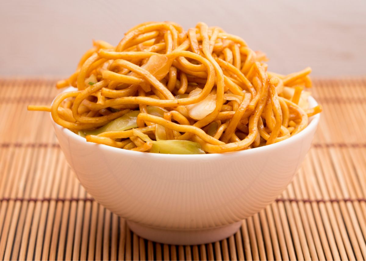 Chow Mein noodles piled high in a white bowl with onion and celery.