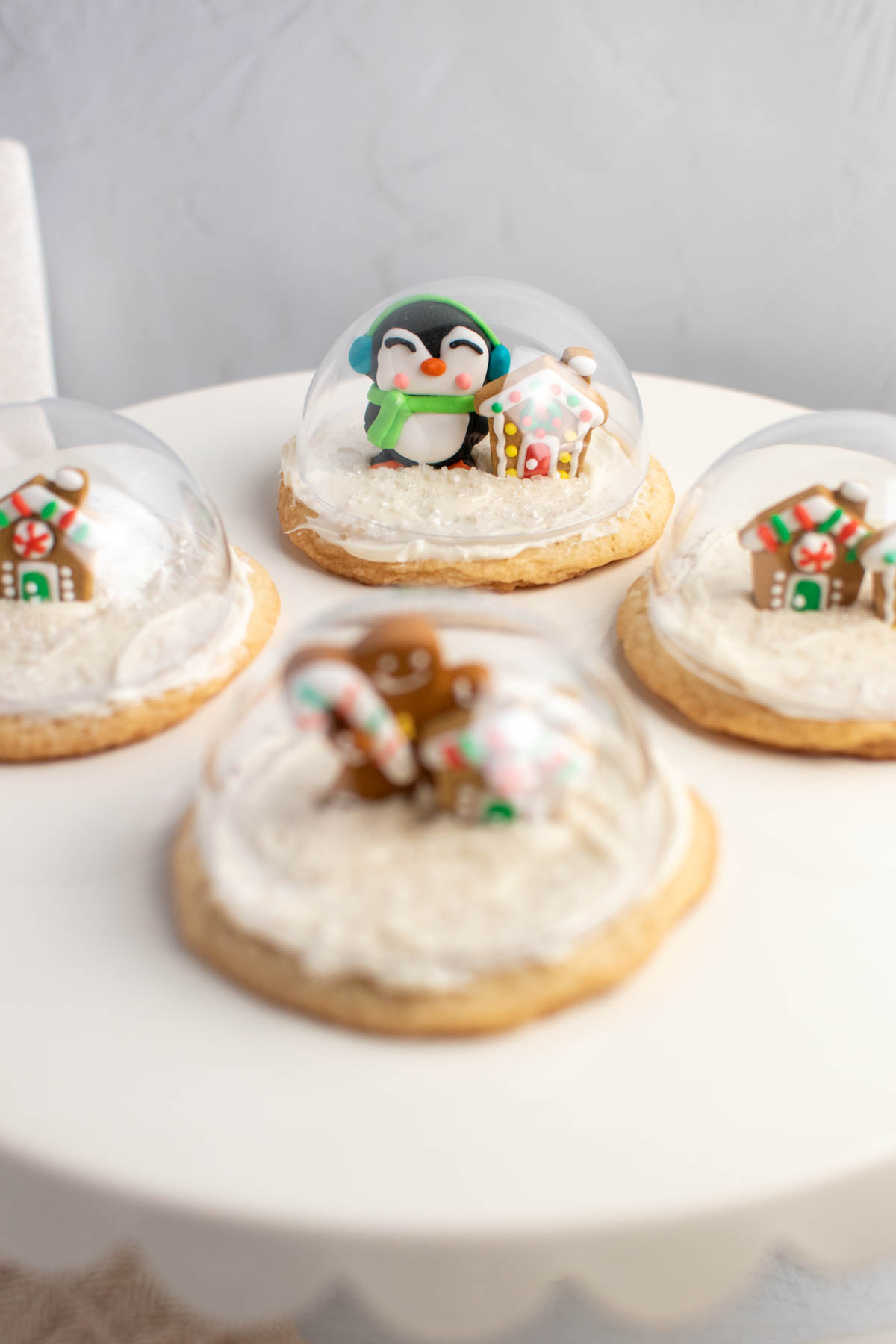 Christmas sugar cookies with icing characters and snow globe tops on white cake stand.