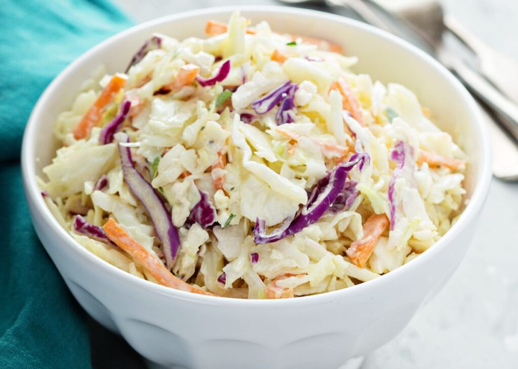 Large white bowl filled with Cole slaw made with carrots and purple and green cabbage.