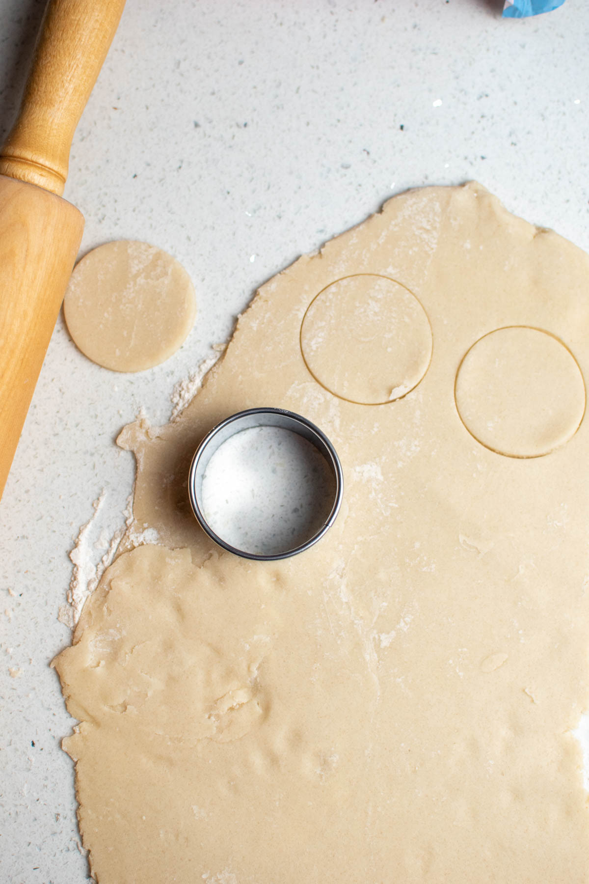 Rolled cookie dough with circles cut out and cookie cutter on dough.
