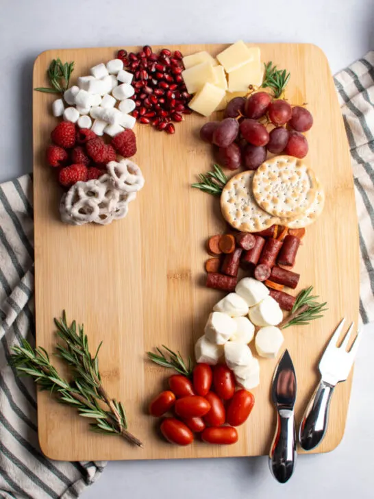 Candy cane charcuterie board with different red and white food and fresh rosemary on table.