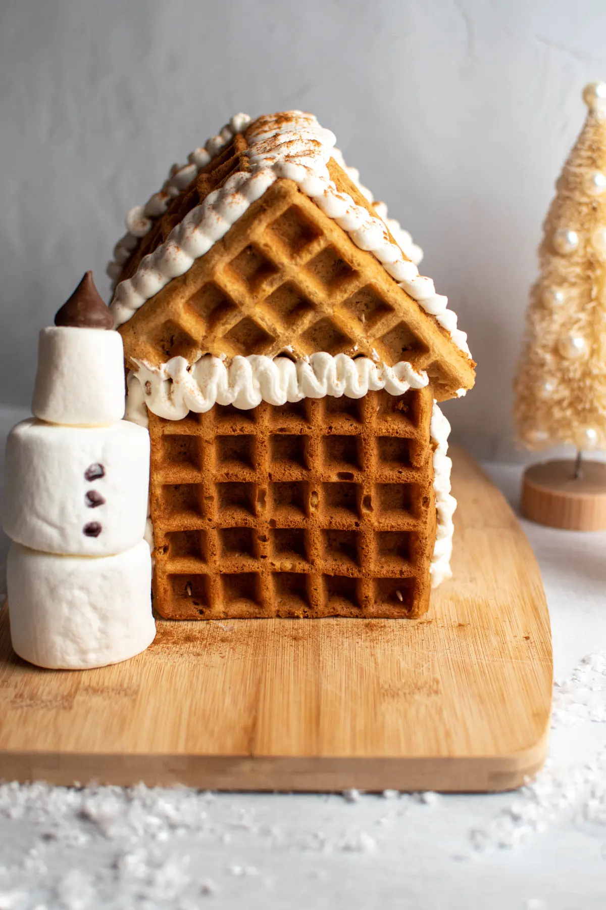 Waffle gingerbread house with whipped cream and marshmallow snowman in front.