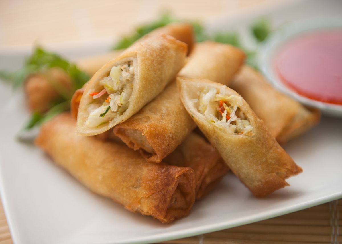 Several whole and cut egg rolls stacked on a white serving platter.