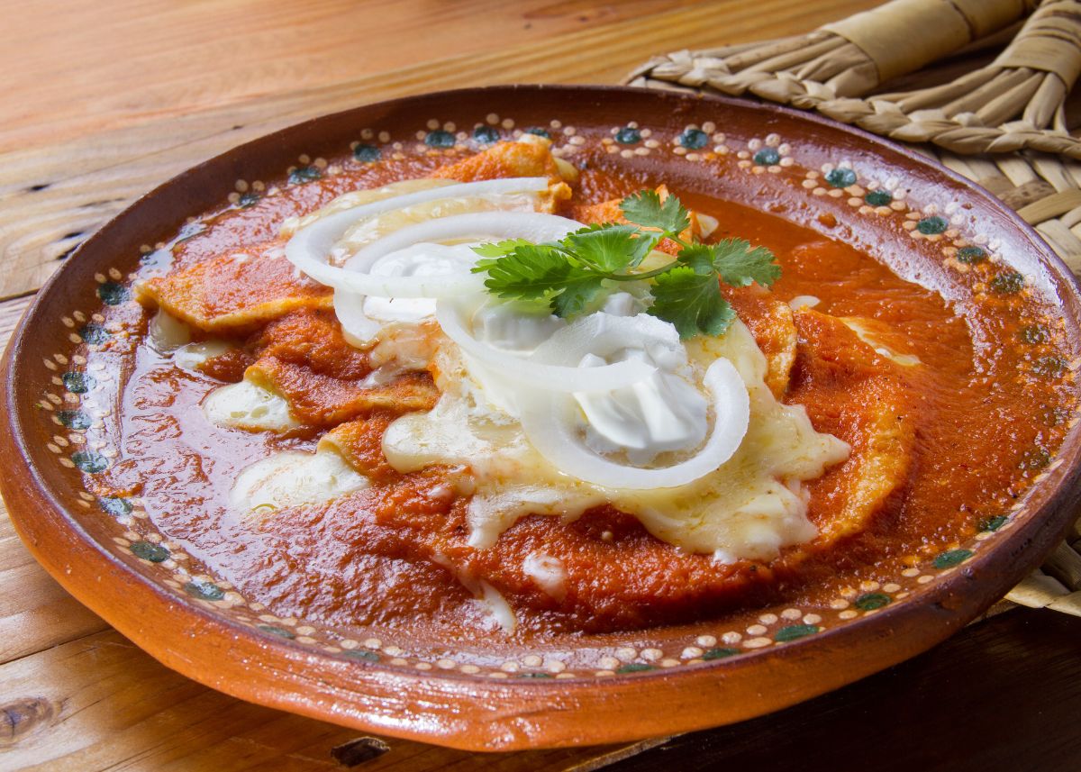 A large plate of enchiladas topped with red enchilada sauce, cheese, and green garnish.