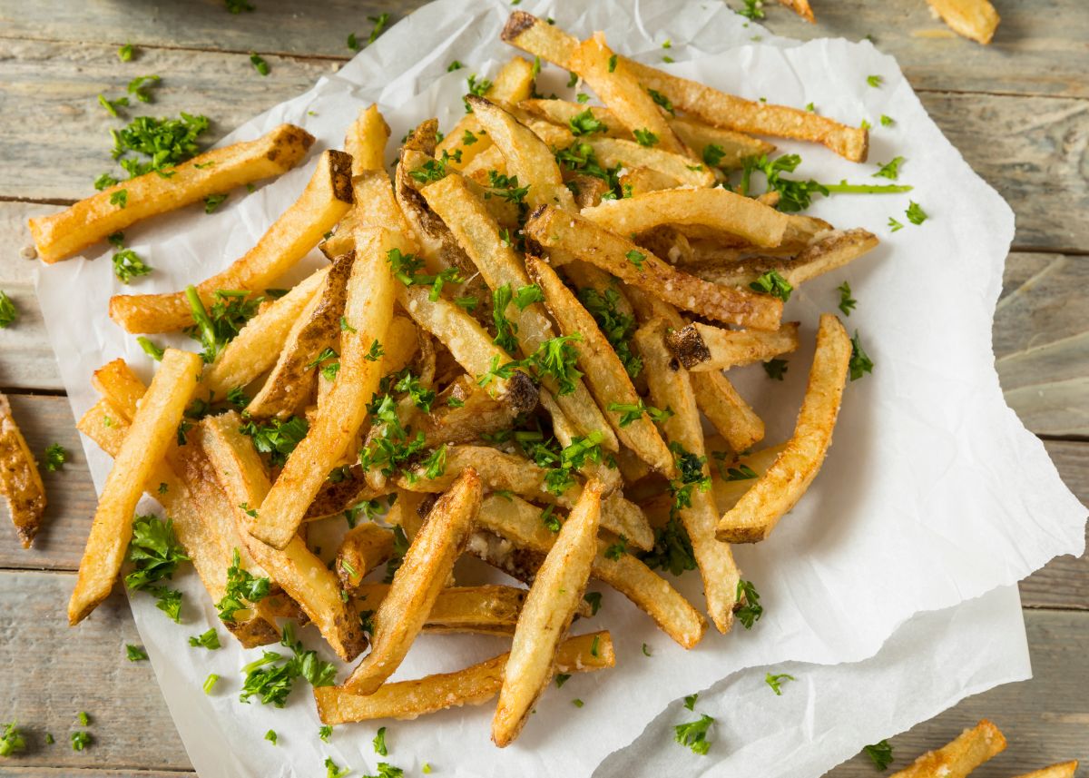 A large pile of homemade French fries with green garnish on parchment paper.