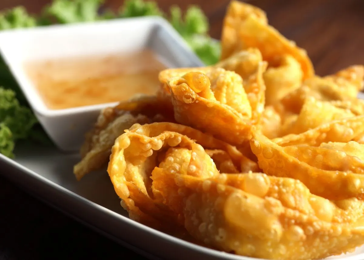 Several fried wontons on a serving platter with a dipping sauce and green garnish.