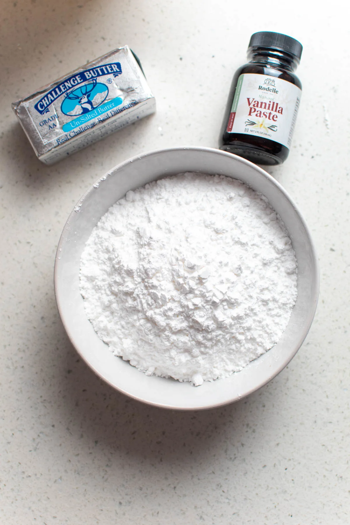 Frosting ingredients on countertop including powdered sugar, butter, and vanilla paste.