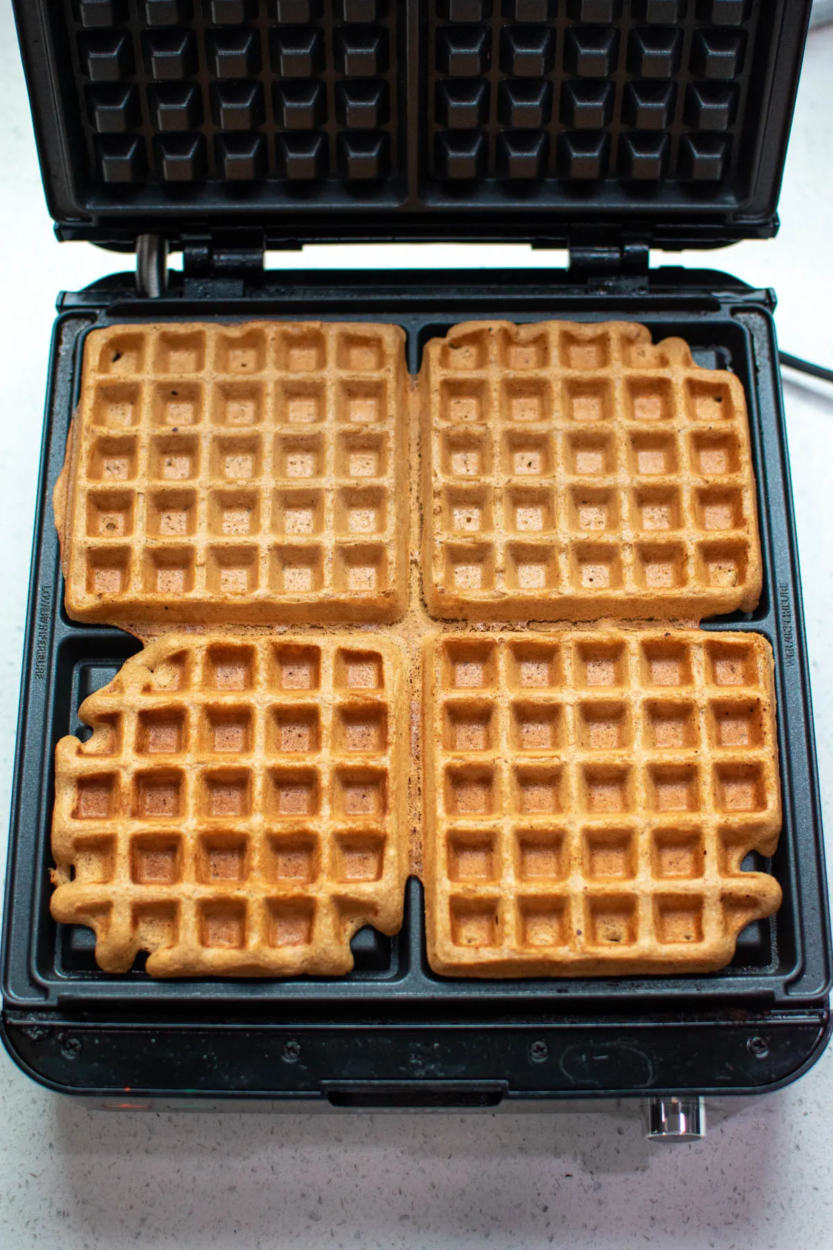 Square waffle iron with 4 cooked gingerbread waffles.