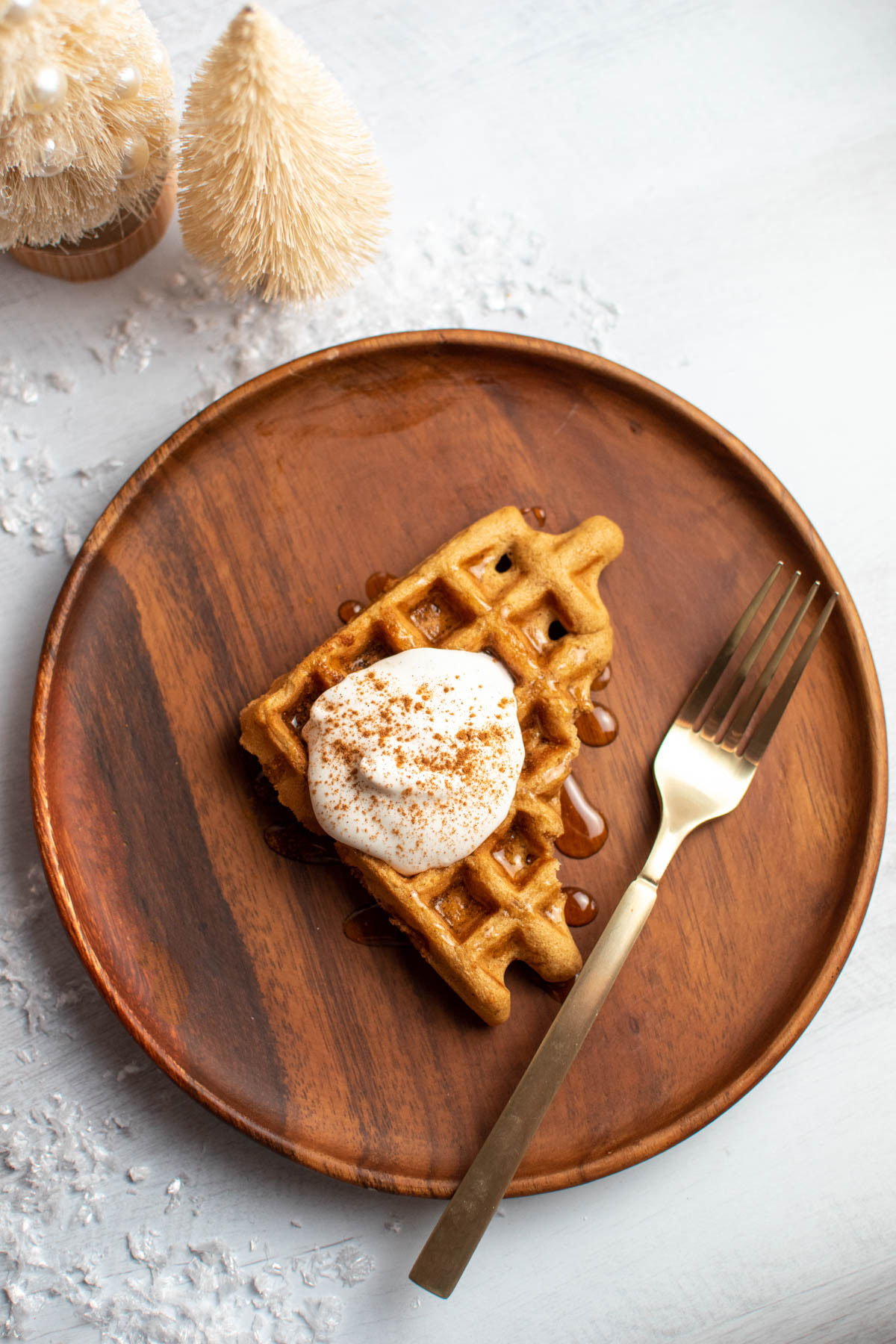 Wood plate with triangle gingerbread waffle with whipped cream and gold fork all on table.