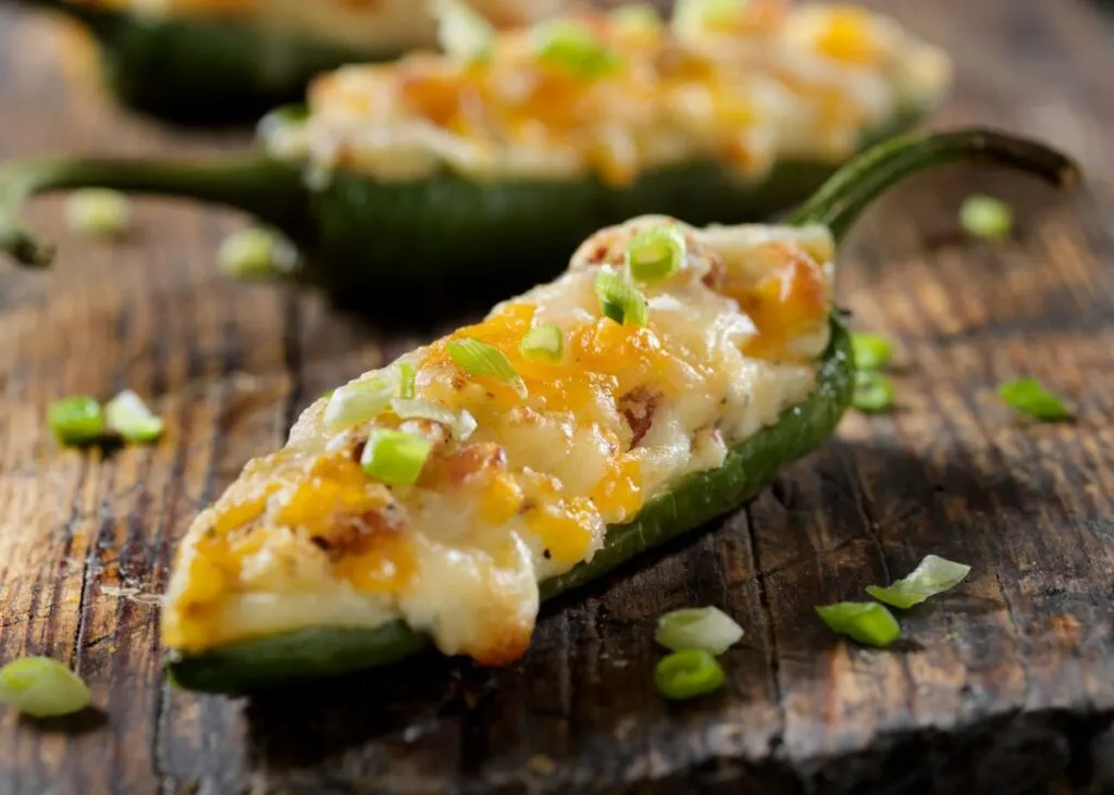 Close up of jalapeno peppers with melted cheese and green garnish.