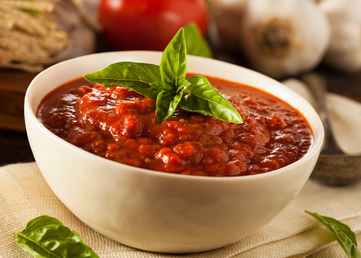 A large cream bowl filled with marinara sauce topped with green garnish.