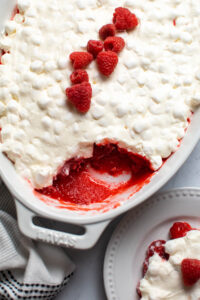 White baking dish with raspberry Jello salad and marshmallow topping with small piece removed.