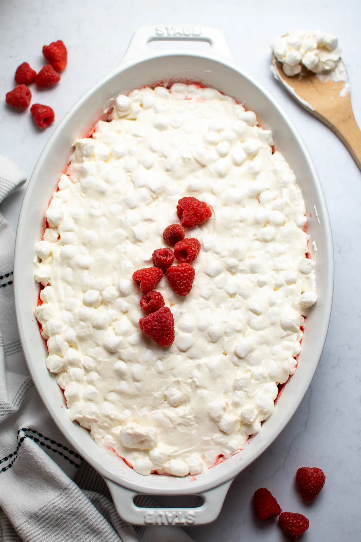White baking dish with raspberry jello salad, marshmallow topping, and fresh raspberries.
