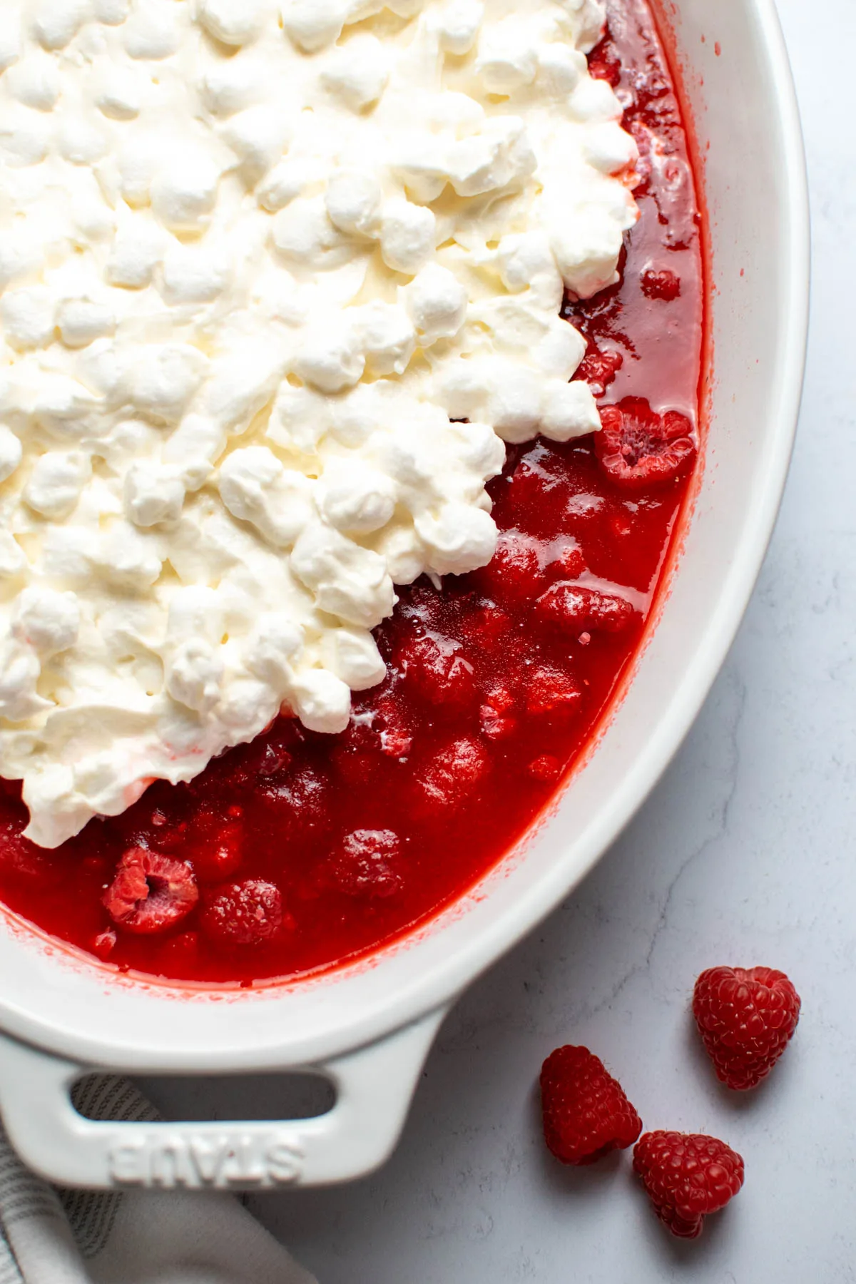 White baking dish with marshmallow topping partially covering raspberry Jello.