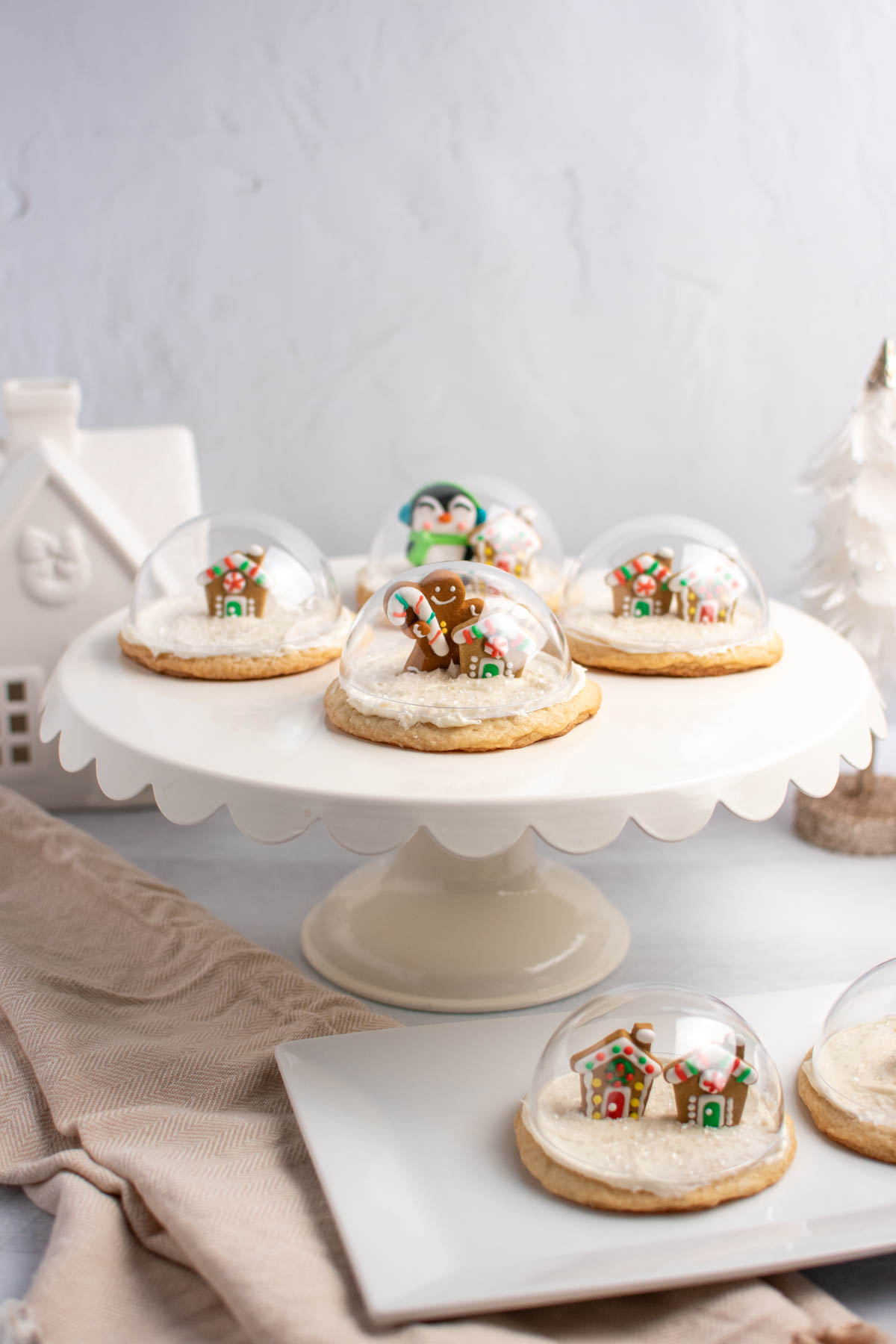 Snow globe sugar cookies with frosting decorations on white cake stand and white platter.