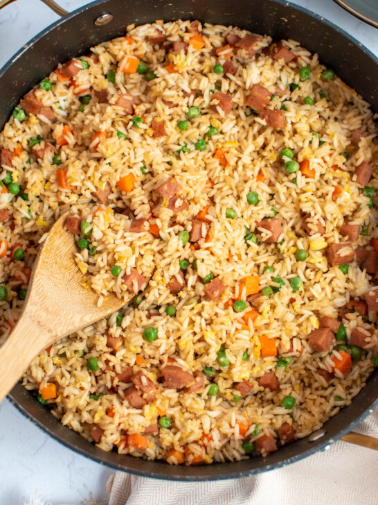 Large black skillet full of Spam fried rice with peas and carrots and wood spoon.