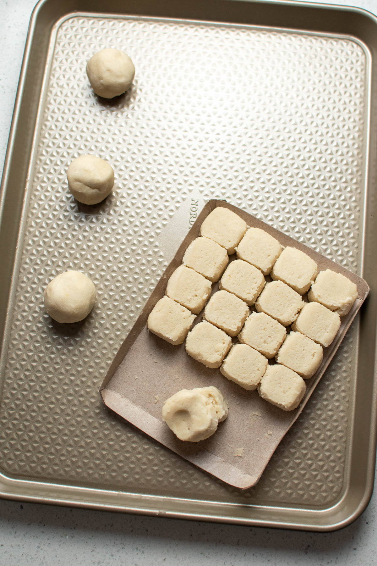 Sugar cookie dough balls on gold baking sheet and cardboard tray.