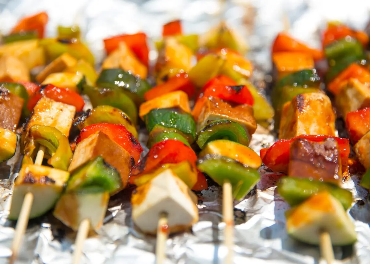 Several vegetable kebab skewers over aluminum foil with zucchini, bell pepper, and squash.
