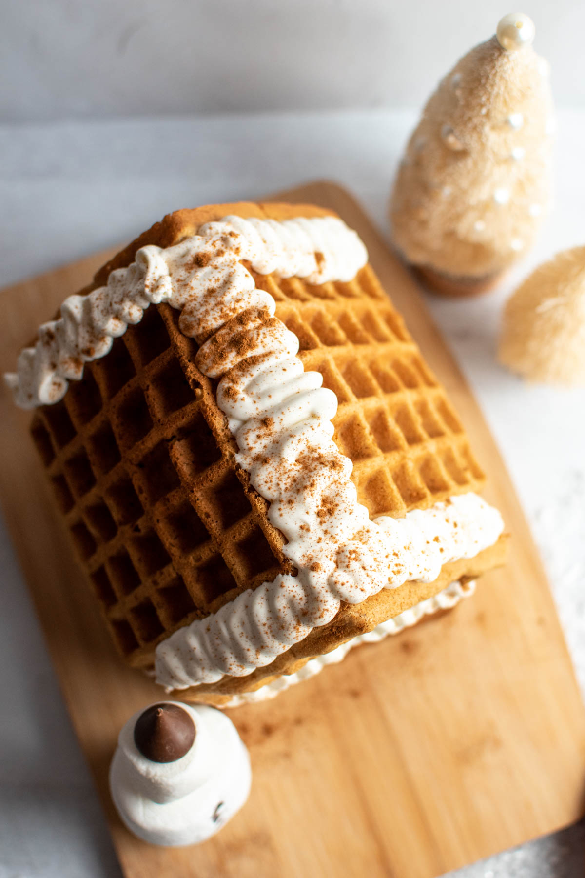 The top of a waffle gingerbread house decorated with whipped cream and cinnamon on wood cutting board.