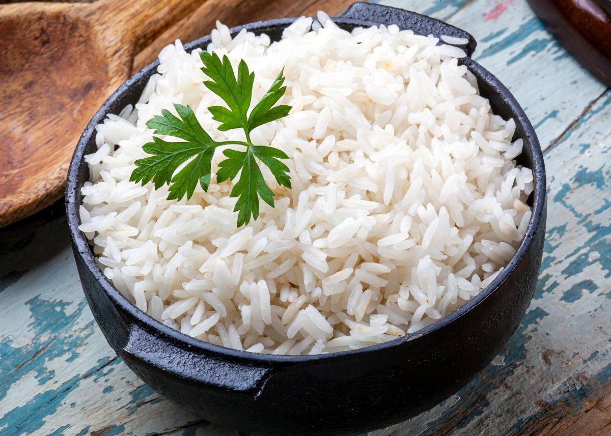 A black cast iron pot filled with cooked white rice with green garnish on top.