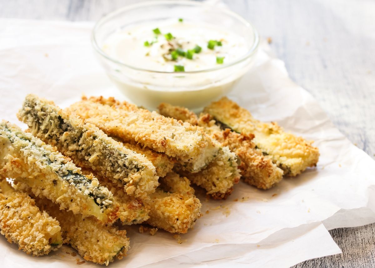 Thick zucchini fries with panko crust next to bowl of dip.