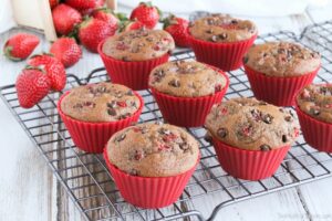 Chocolate chip muffins with strawberries in red cupcake liners, cooling on baking rack.