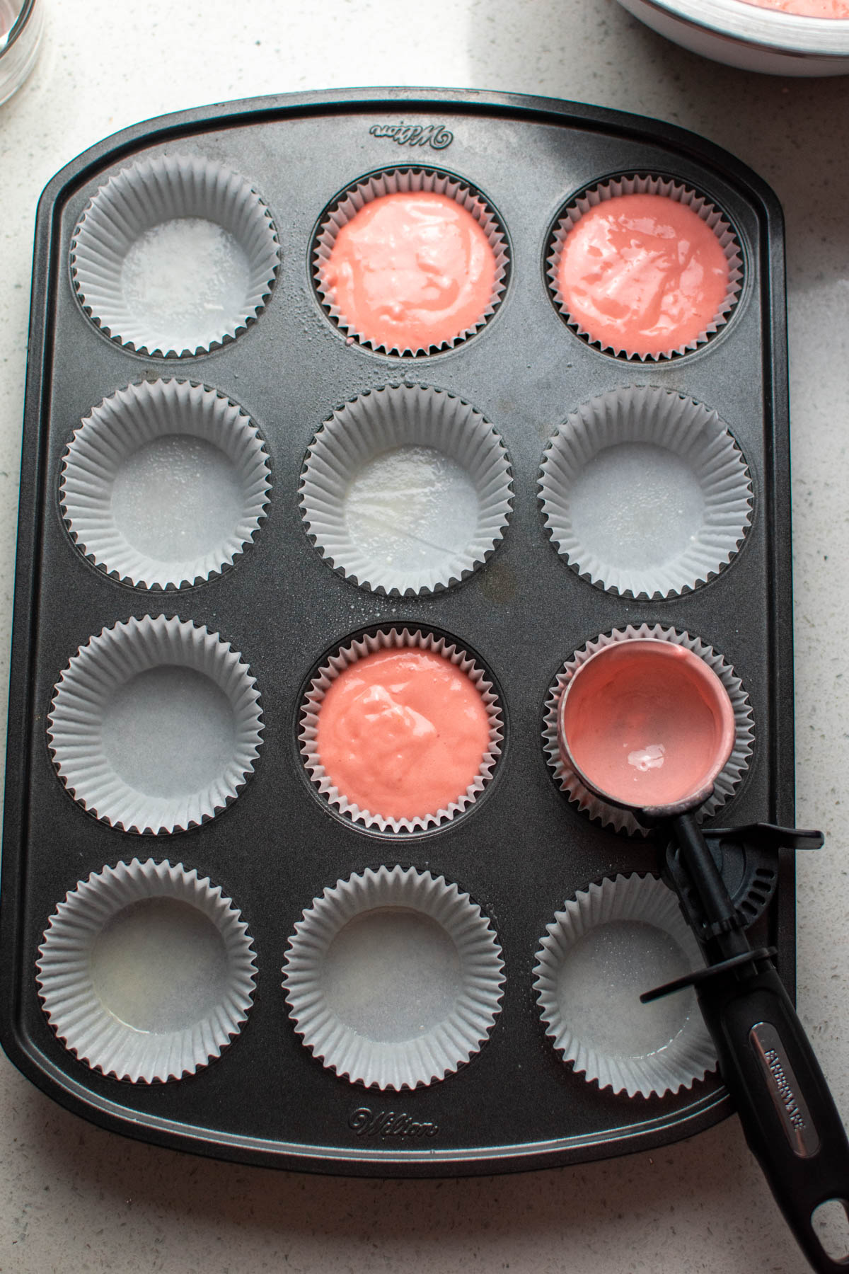 Pink cupcake batter in a few liners of cupcake tin with other liners empty.