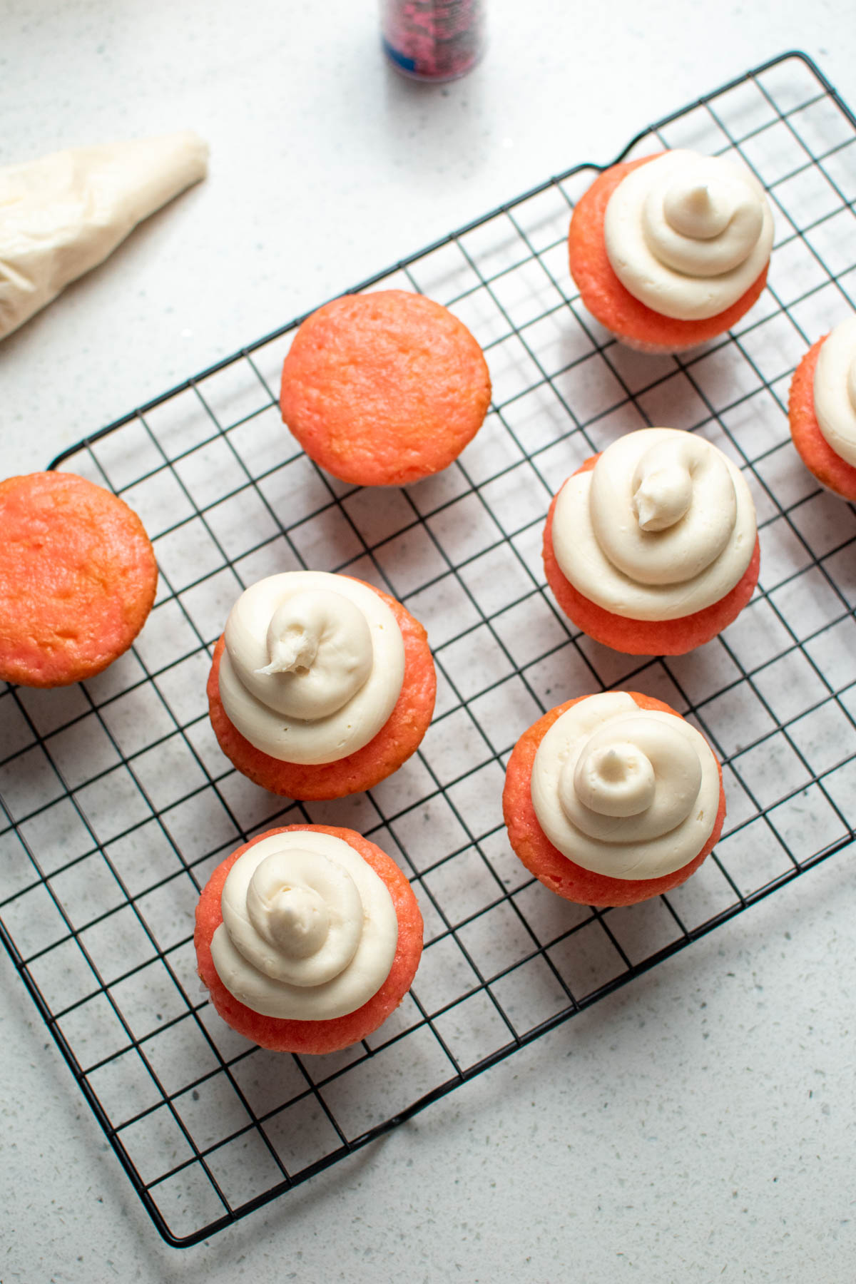 Cream cheese frosted strawberry cupcakes on baking rack.