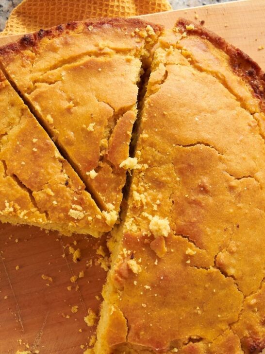 A large sliced round loaf of cornbread with pieces missing on a cutting board.