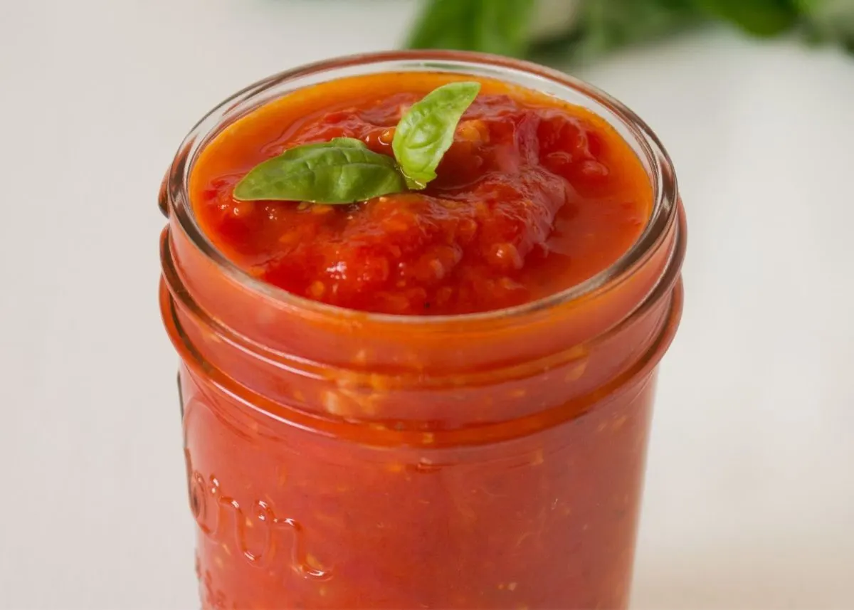 Clear glass jar filled with fresh marinara sauce with green basil garnish.