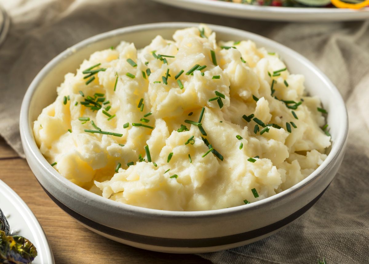 A large bowl of buttery mashed potatoes with green garnish on top sitting on wood table.